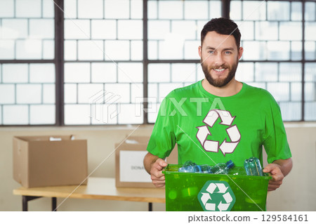 Man standing holding green recycling bin with bottles in community center sorting area, copy space 129584161