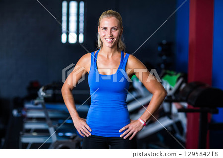 Woman standing at fitness studio by weight bench wearing blue tank top and fitness tracker Woman standing at fitness studio by weight bench wearing blue tank top and fitness tracker 129584218