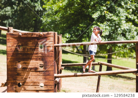 Child girl balancing on thick wooden beam at park playground using rope railings, copy space Child girl balancing on thick wooden beam at park playground using rope railings, copy space 129584238