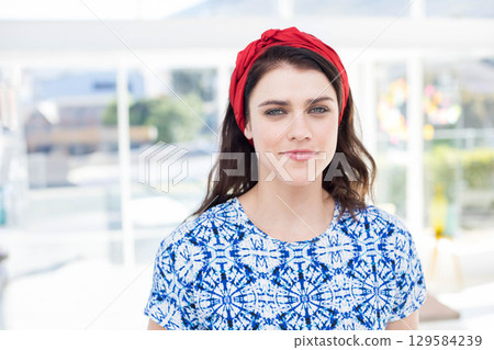 Woman in twenties standing on sunlit terrace wearing red headband and blue blouse by white railing Woman in twenties standing on sunlit terrace wearing red headband and blue blouse by white railing 129584239