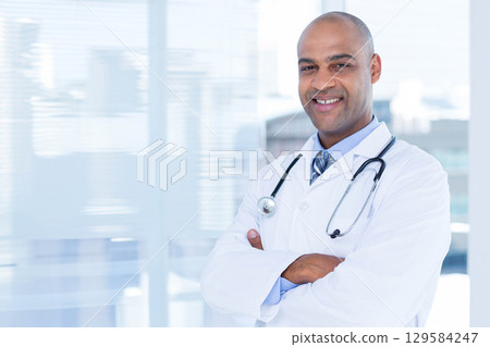 African American male doctor standing in clinic by blinds in lab coat, tie, stethoscope, copy space African American male doctor standing in clinic by blinds in lab coat, tie, stethoscope, copy space 129584247