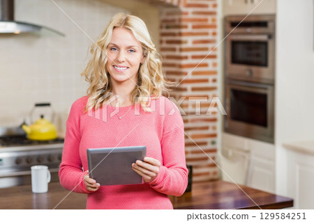 Woman holding digital tablet and checking recipes in modern kitchen near yellow kettle with mug 129584251