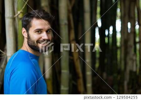 Man standing and smiling back over shoulder in bamboo grove wearing blue athletic top, copy space Man standing and smiling back over shoulder in bamboo grove wearing blue athletic top, copy space 129584255