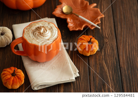 Cozy pumpkin latte in a pumpkin-shaped mug with whipped cream and spices, surrounded by autumn decor. 129584481