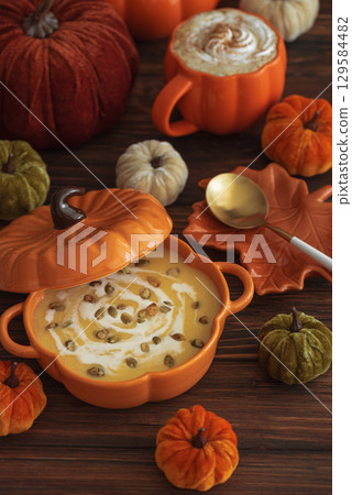 Autumnal lunch with pumpkin soup in a pumpkin-shaped bowl, pumpkin latte, croutons and festive decor on dark wooden table 129584482