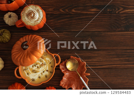 Autumnal lunch with pumpkin soup in a pumpkin-shaped bowl, pumpkin latte, croutons and festive decor on dark wooden table. Copy space 129584483