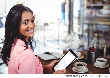 Adult Chinese woman holding blank-screen tablet and writing in notebook on cafe table, copy space 129584517