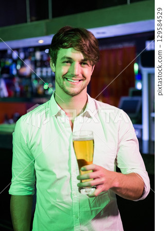 Man holding pint glass at pub counter under green lights, showing liquor bottles and POS terminal Man holding pint glass at pub counter under green lights, showing liquor bottles and POS terminal 129584529