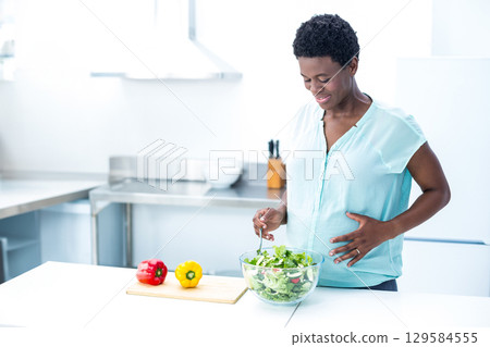 African American woman stirring green salad in bowl on kitchen counter with peppers, copy space African American woman stirring green salad in bowl on kitchen counter with peppers, copy space 129584555