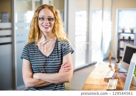 Mid adult woman in glasses and striped t-shirt standing arms crossed at office desk with mannequin 129584561