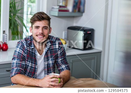 Man sitting at kitchen table holding ceramic mug near toaster and fruit bowl gazing at window 129584575