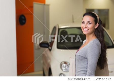Woman standing in front of white car at showroom wearing headband carrying tote bag, copy space 129584576