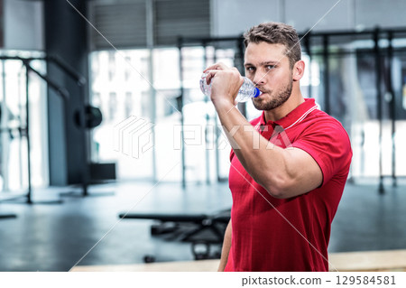Man wearing red polo shirt drinking from water bottle while pausing in weight area, copy space 129584581