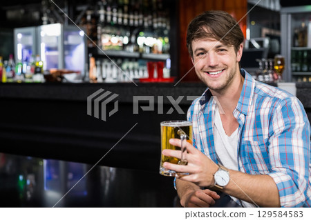 Smiling man raising glass beer mug while sitting on glossy bar counter at pub, copy space Smiling man raising glass beer mug while sitting on glossy bar counter at pub, copy space 129584583