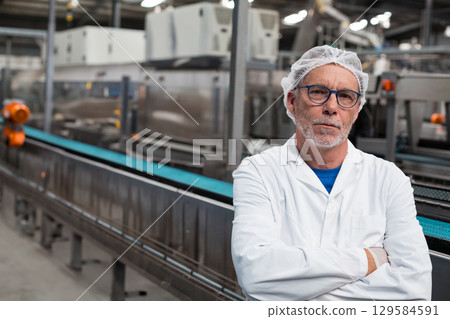 Senior man wearing protective attire inspecting conveyor belt in manufacturing plant, copy space 129584591