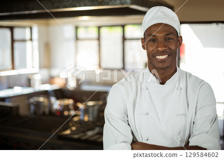 African American male chef in chef coat standing in restaurant kitchen beside stove, copy space 129584602
