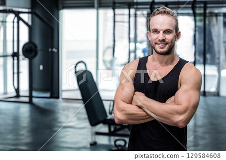 Muscular man in tank top standing with arms crossed at gym near weight machines, copy space Muscular man in tank top standing with arms crossed at gym near weight machines, copy space 129584608