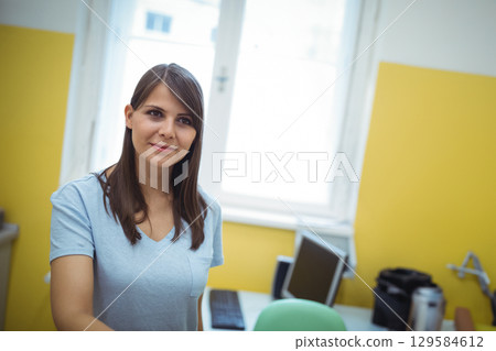 Woman standing in compact office, holding stainless steel flask near monitor, copy space 129584612