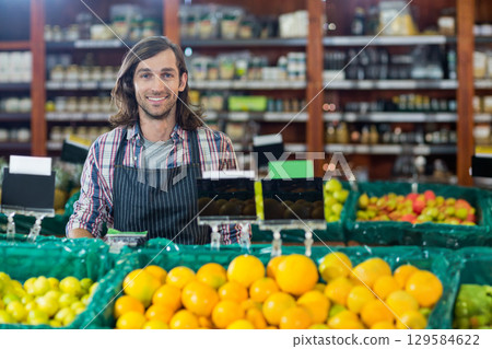 Mid adult male vendor standing behind green crates of oranges at grocery store with chalkboard tags Mid adult male vendor standing behind green crates of oranges at grocery store with chalkboard tags 129584622