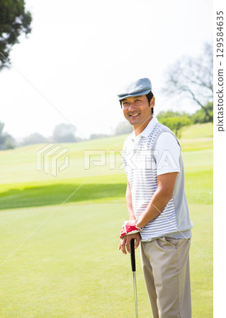 Asian man standing on putting green wearing polo shirt holding putter with golf glove, copy space 129584635