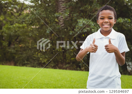 Smiling African American boy wearing white shirt in park giving thumbs up to camera, copy space Smiling African American boy wearing white shirt in park giving thumbs up to camera, copy space 129584697