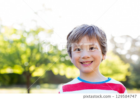 Male child standing and smiling at park with red and white striped T-shirt under bright sunlight 129584747