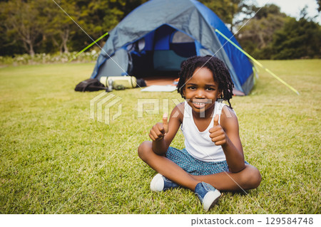 African American boy sitting cross-legged on green lawn beside gray tent with sleeping pad and bag African American boy sitting cross-legged on green lawn beside gray tent with sleeping pad and bag 129584748