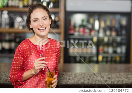Female patron standing at bar counter holding glass of drink near refrigerated display, copy space 129584772
