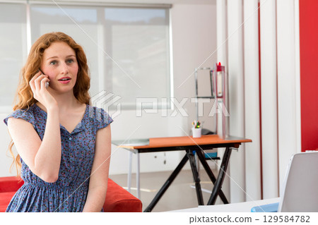 Woman talking on smartphone next to adjustable work table with orange mat in creative workspace 129584782