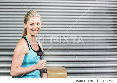 Woman in thirties lifting hexagonal dumbbell at gym beside wooden box in turquoise top, copy space 129584790