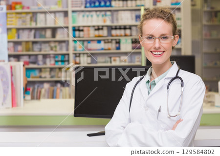 Female pharmacist standing behind counter in pharmacy using monitor with stethoscope, copy space 129584802