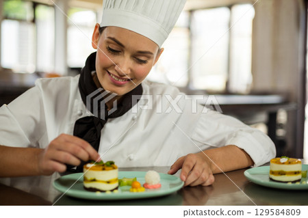 Female chef wearing white uniform at pastry station plating layered desserts on pale blue plates Female chef wearing white uniform at pastry station plating layered desserts on pale blue plates 129584809