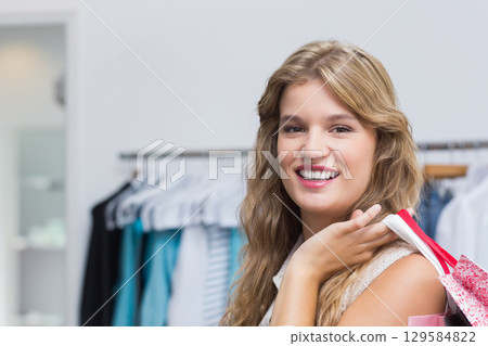 Female shopper in twenties smiling and holding pink shopping bags at shop with clothing rack Female shopper in twenties smiling and holding pink shopping bags at shop with clothing rack 129584822