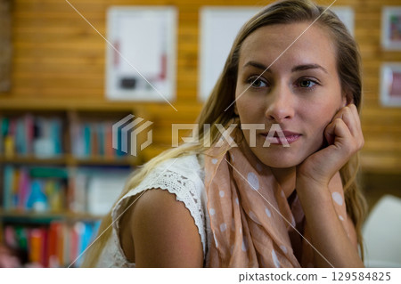 Female supporting chin gazing at library wood panel table featuring shelves and scarf, copy space Female supporting chin gazing at library wood panel table featuring shelves and scarf, copy space 129584825
