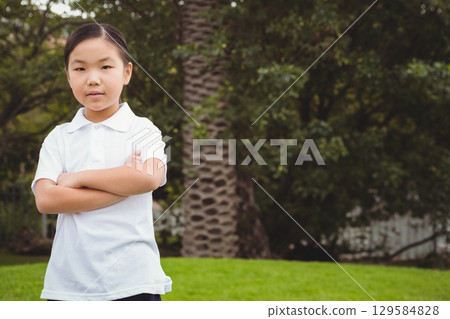Chinese girl standing with arms crossed on lawn in backyard by palm tree, white picket fence 129584828