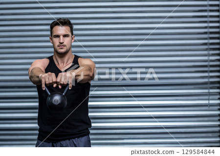 Mid adult man holding cast-iron kettlebell in sportswear at industrial gym, copy space 129584844