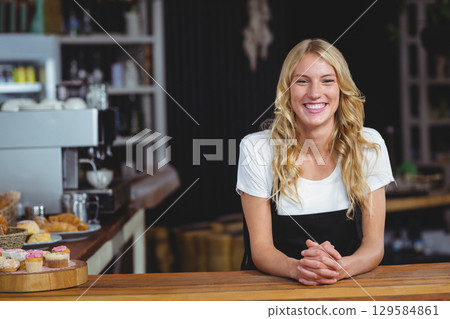Woman barista standing behind wooden countertop in cafe, serving cupcakes and espresso, copy space Woman barista standing behind wooden countertop in cafe, serving cupcakes and espresso, copy space 129584861