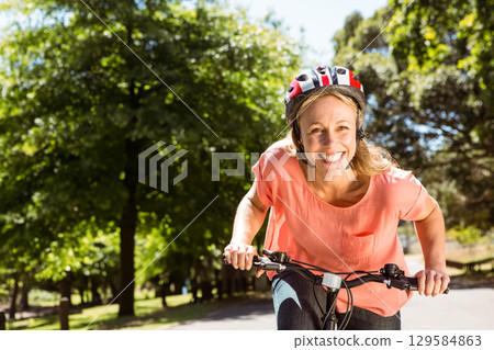 Mid adult female cyclist pedaling bicycle along park path wearing red-and-white helmet, copy space 129584863