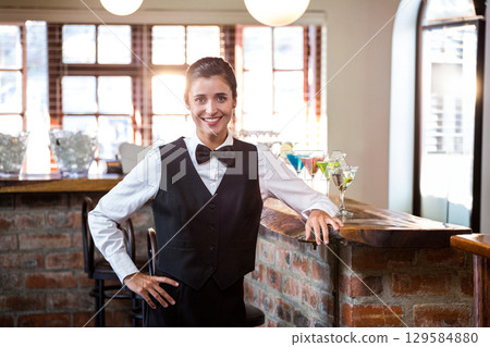 Female bartender wearing uniform serving at brick counter offering colorful cocktails Female bartender wearing uniform serving at brick counter offering colorful cocktails 129584880