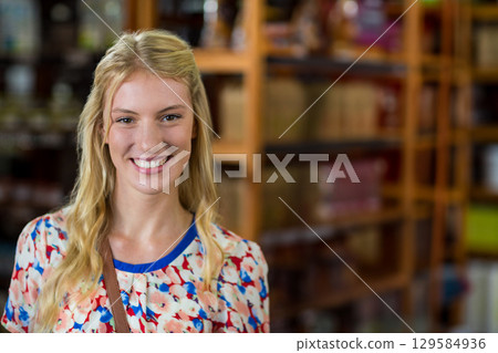 Woman standing in aisle wearing leather crossbody bag examining shelves filled with jars and boxes 129584936