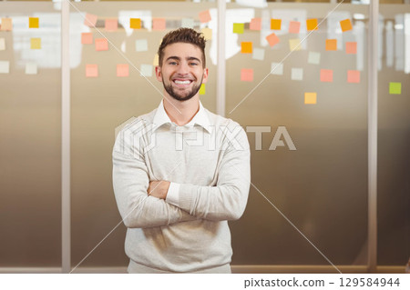 Male office worker standing in workspace brainstorming using colorful sticky notes on glass wall 129584944
