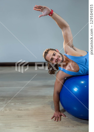 Man stretching side on blue stability ball in home gym wearing athletic top, copy space Man stretching side on blue stability ball in home gym wearing athletic top, copy space 129584955