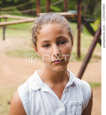 Preteen girl standing wearing white blouse with lace at playground by wooden bench Preteen girl standing wearing white blouse with lace at playground by wooden bench 129584964