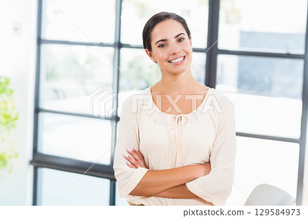 Professional woman in blouse standing with arms crossed at office by steel frame window and plant 129584973