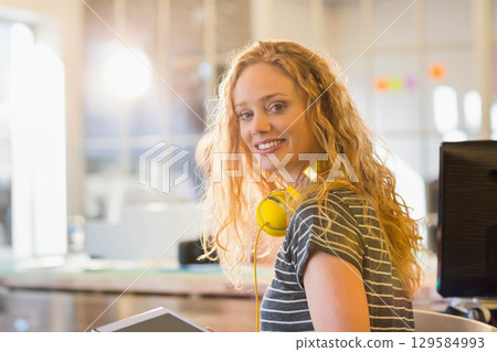 Woman smiling while holding tablet and wearing yellow headphones in modern office with sticky notes 129584993