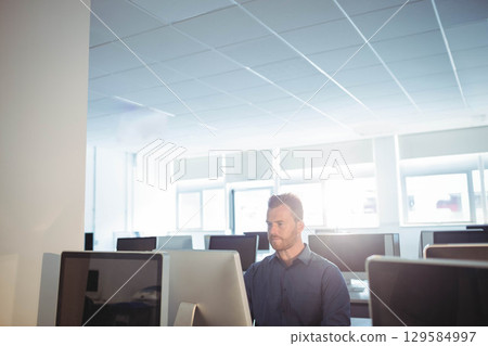 Man wearing dark button-up shirt working at desk in modern office on computer monitors Man wearing dark button-up shirt working at desk in modern office on computer monitors 129584997