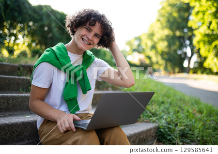 Curly-haired teen sitting on the steps in the park and having a video call Curly-haired teen sitting on the steps in the park and having a video call 129585641