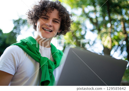 Curly-haired teen sitting on the steps in the park and having a video call Curly-haired teen sitting on the steps in the park and having a video call 129585642