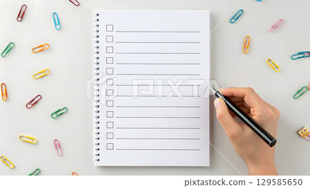 Creating a checklist on a notebook with colorful clips scattered around the desk 129585650