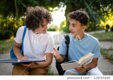 Two teens sitting in the park and studying together Two teens sitting in the park and studying together 129585690
